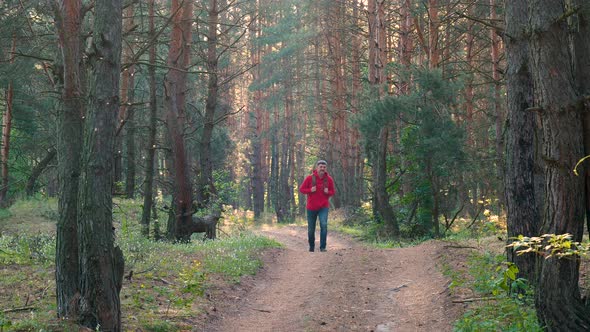 A Man with a Backpack Walks Along a Forest Road