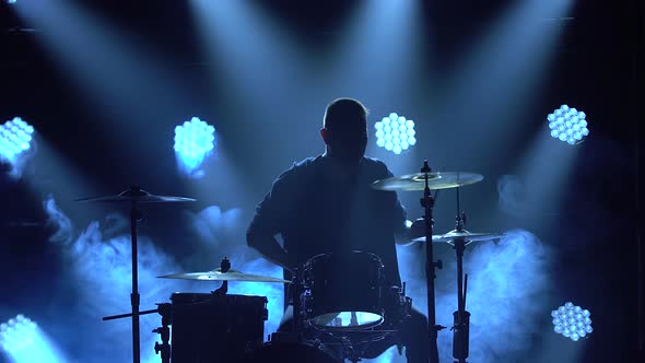 Silhouette Drummer Playing on Drum Kit on Stage in a Dark Studio with Smoke and Neon Lighting