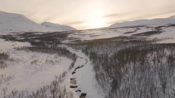 Cabin on frozen river bank in remote wilderness of snowy landscape; drone