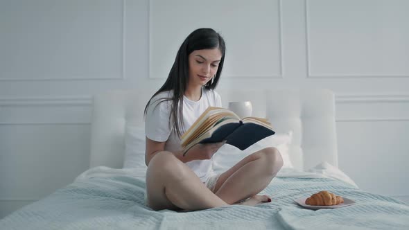 Girl Reading Book in Bed and Drinking Coffee