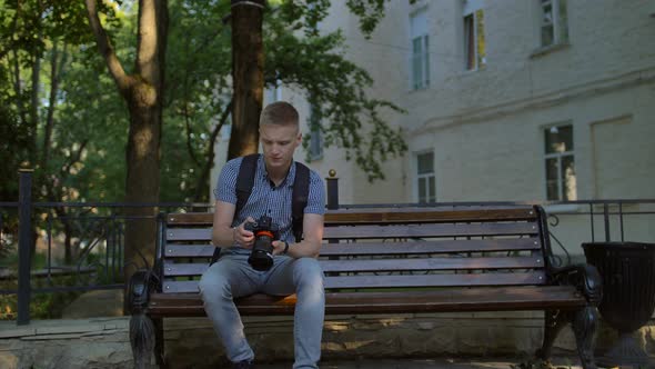 Tourist Sits on a Bench and Scrolls at the Photographs Taken on a Digital Expensive Big Camera.