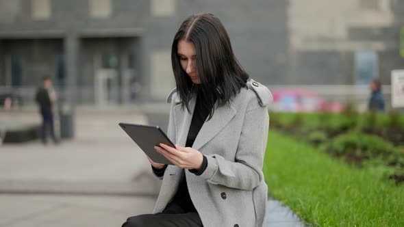Adult Woman is Using Tablet with Internet on Street Sitting Outdoors and Messaging in Networks