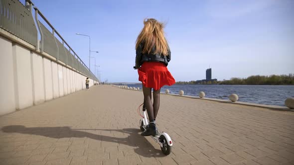 Young Blonde Woman Rides Electric Scooter