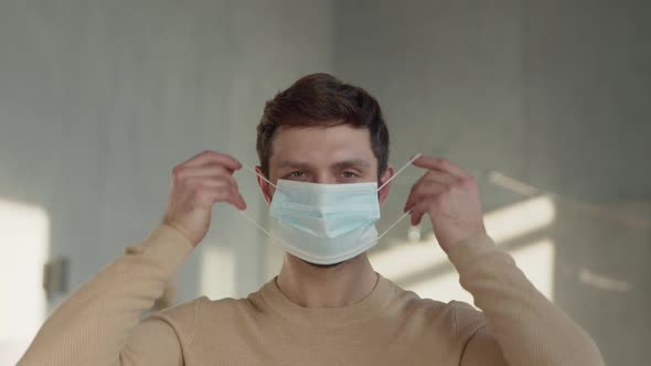 A young man puts on a blue medical mask