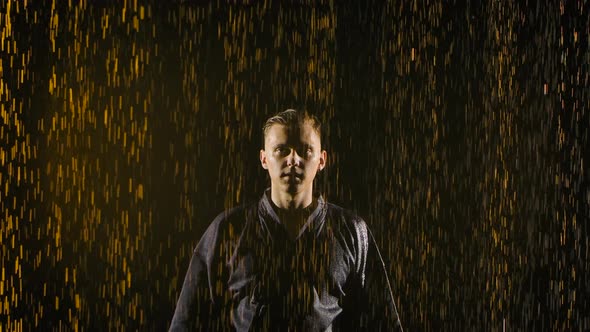 Portrait of Young Man Posing with Fighting Bamboo Sword in His Hands in Rain on Dark Studio