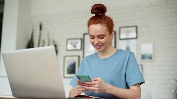 Portrait of Happy Cheerful Redhead Young Woman Using Cell Phone at Home Office