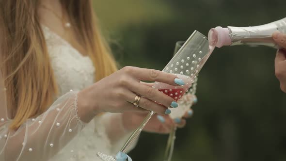 Groom Pours Pink Champagne Into the Glasses Held By the Bride