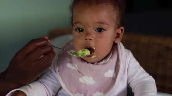 A baby girl being fed while in a highchair.