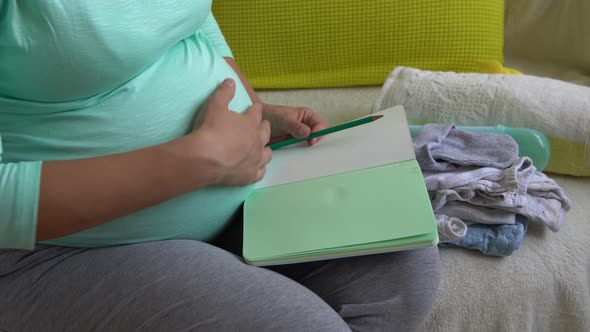 Cute Pregnant Woman Writing Packing List for Maternity Hospital With Notebook Prepares Bags