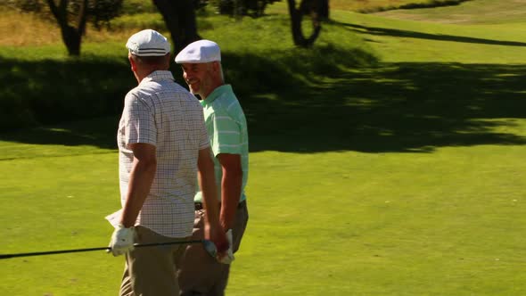 Two Male Friends Chatting and Walking on the Golf Course Past their Kart