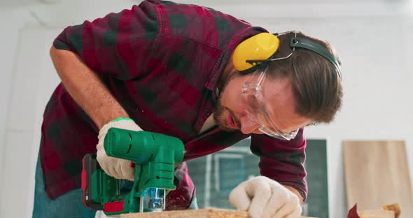 Young Carpenter Cuts an Osb Board with a Jigsaw Craftsman's Hands in Cloth Protective Gloves The