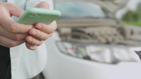 Close Up Hand of Woman Using Smartphone and Blur of Her Broken Car Parking on the Road. Contacting