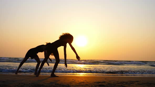 Silhouette of Sporty Young Women Practicing Acrobatic Element on the Beach