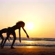Silhouette of Sporty Young Women Practicing Acrobatic Element on the Beach - VideoHive Item for Sale