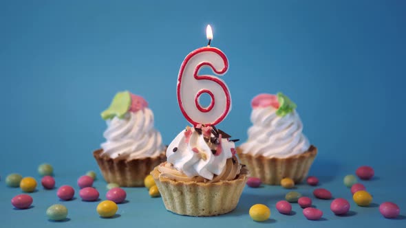 Cake Birthday Cupcake with a Burning Candle Number Six 6 on a Blue Background