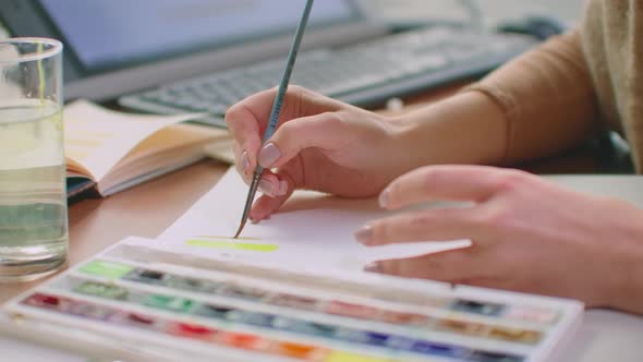 A Young Woman with a Brush and Paints Chooses a Suitable Shade for the Logo Design or Walls