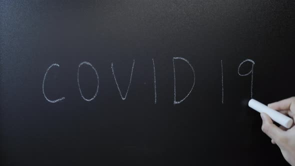 Hand writes Covid 19 on chalkboard.