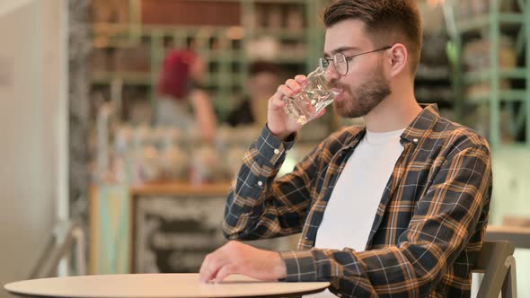 Pensive Young Man Drinking Water in Cafe