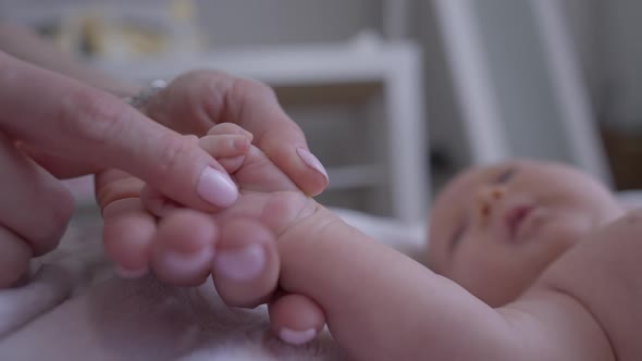 Closeup Female Finger Stroking Newborn Baby Hand with Blurred Little Girl Lying at Background