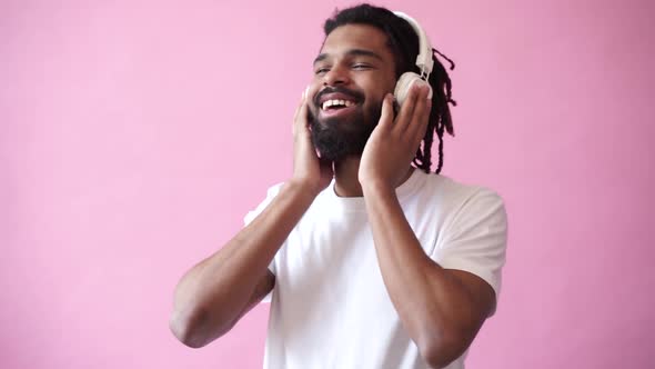 Young attractive African man listens to music and dances in white headphones