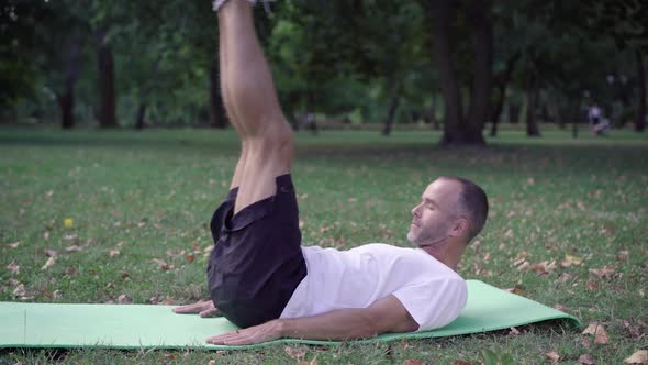 Side View of Strong Athletic Sportsman Lying on Exercise Mat Raising Legs and Head. Wide Shot