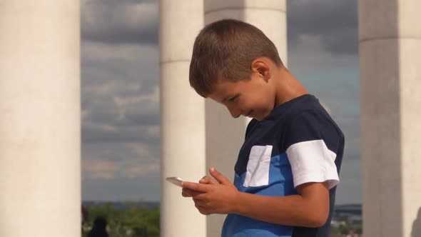 A Little Boy Is Watching at the Phone in His Hands