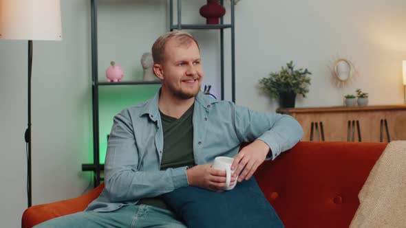 Portrait of Young Adult Man Sitting on Couch Relaxing at Home Room Drinking Enjoy Tea or Coffee