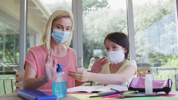 Mother and daughter wearing face masks sanitizing their hands at home