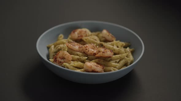 Slow Motion Handheld Shot of Pesto Penne with Fried Shrimps in Blue Bowl on Black Background