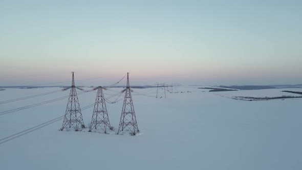 Aerial Drone View on Power Lines Over the Snowy Field at Sunset