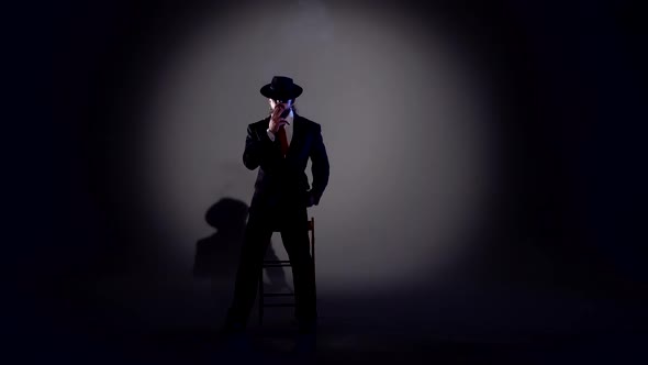 Elegant Man in a Black Hat Is Dancing an Erotic Dance. Spotlight on a Black Background.