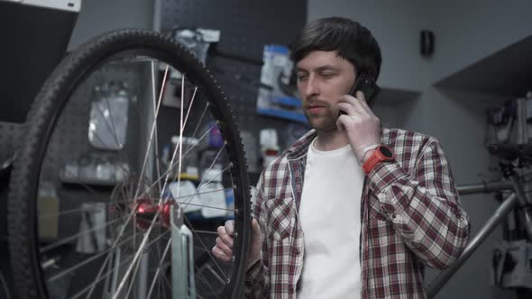 Store Employee Takes Order By Mobile Phone Standing in Bicycle Workshop Near Cycle Wheel