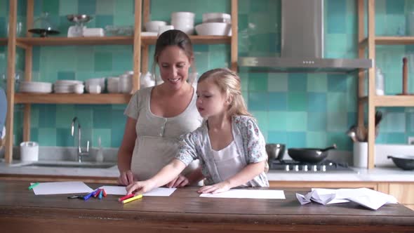 Little girl coloring with her mother in kitchen