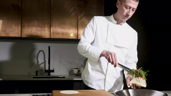 chef in the kitchen puts the filling into a Mexican taco tortilla with tongs.