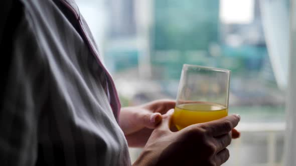 Woman in Striped Pajamas and with a Sleep Mask is Sitting on the Bed in the Bedroom and Drinking