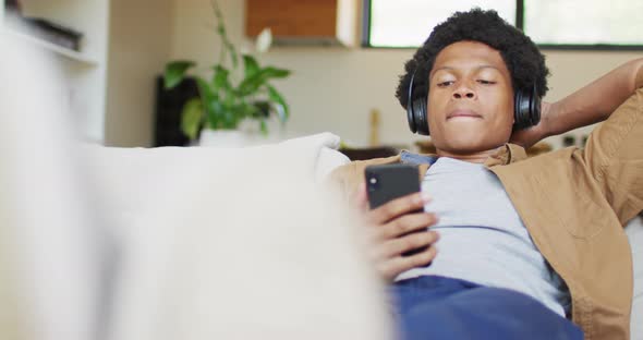 Happy african american man using smartphone and headphones at home