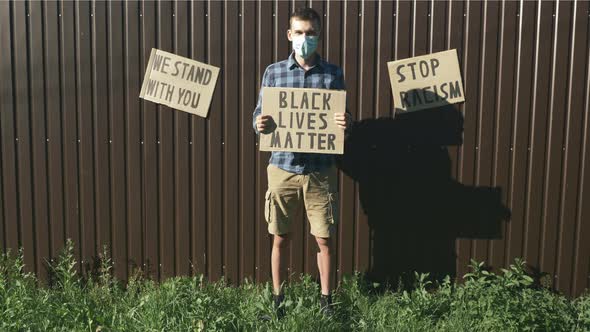Man in protective face mask standing against brown background with poster "Black lives matter"
