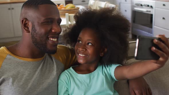 African american daughter and her father taking selfie together sitting on couch smiling