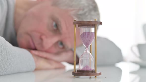 Upset Senior Old Man Looking at Hourglass in Anticipation at Home 
