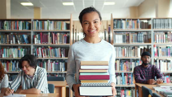 Happy African American Woman Walking in School Library Holding Books Smiling