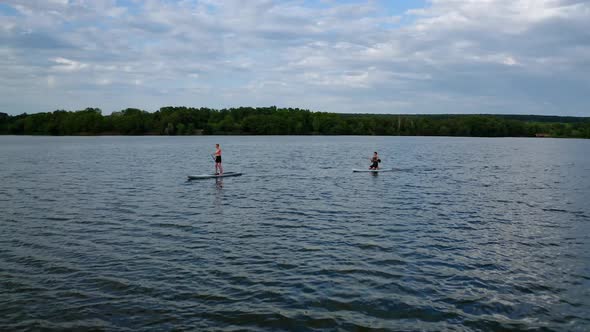 Aerial view of people standing on sup board and swims surfing