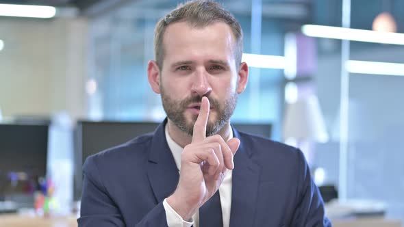 Portrait of Young Businessman Putting Finger on Lips