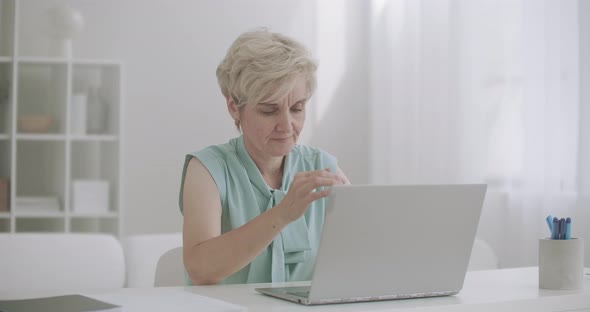 Middle-aged Woman Is Working with Laptop Is Feeling Headache, Touching Forehead By Hands