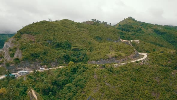 Aerial drone shot tracking horizontally past a mountain in central Cebu with a road carved into the