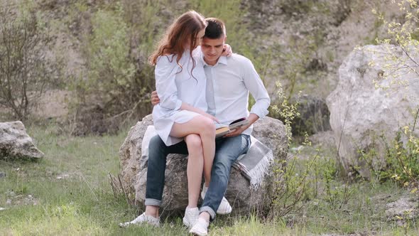 Man and Woman Sitting on Stone and Reading Book Together