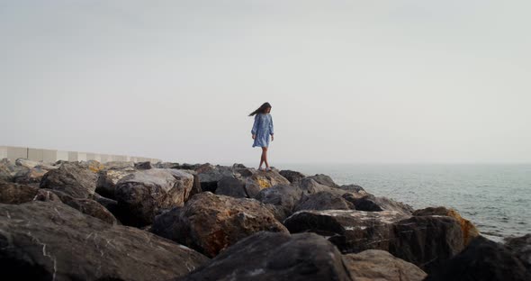 A Young Woman Walks Over Large Boulders Along the Coastline