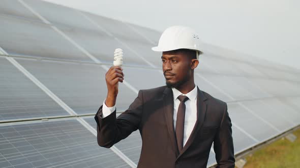 African American Man with Light Bulb in Hand Standing on Field with Rows of