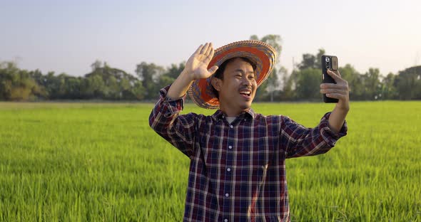 Happy Asian farmer make a video call with family by smartphone at organic rice field.