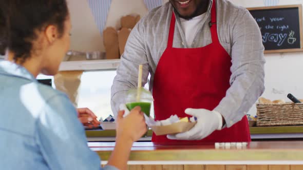 African american man wearing apron serving and fries smoothie to a woman at the food truck