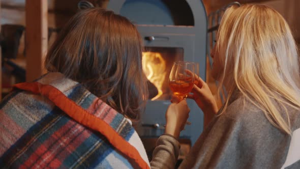 Two Young Women Lesbian Couple Relaxing Near the Fireplace and Drinking Wine in the Cozy Home